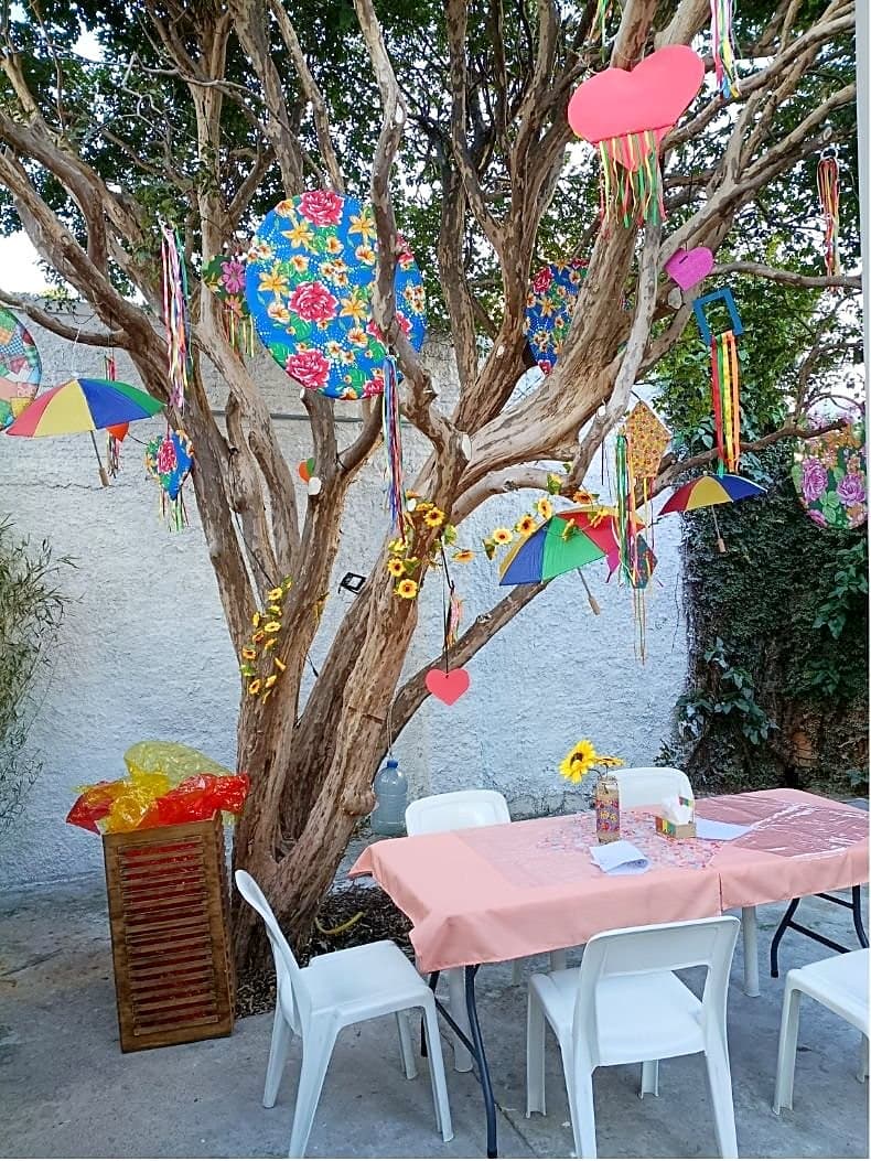 Árvore do quintal da Morada decorada com bandeirinhas, flores, guarda-chuvas coloridos e enfeites da Festa Junina