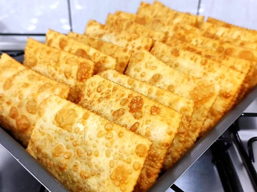 Fileiras de pastéis dourados, recém-fritos, empilhados numa forma
